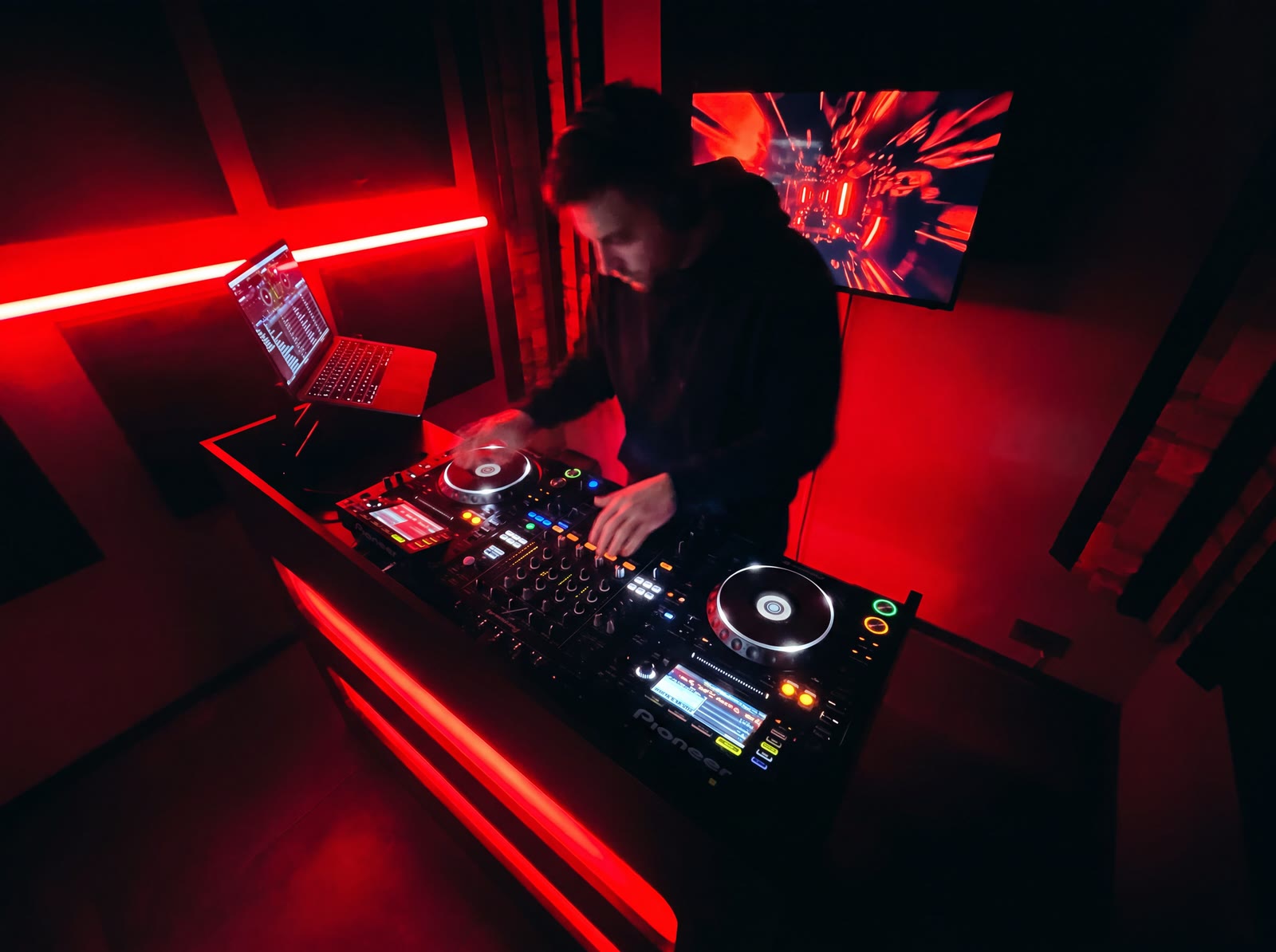 Bovenaanzicht van een dj die mixt op Pioneer CDJ's in een roodverlichte Temple Studios-booth
