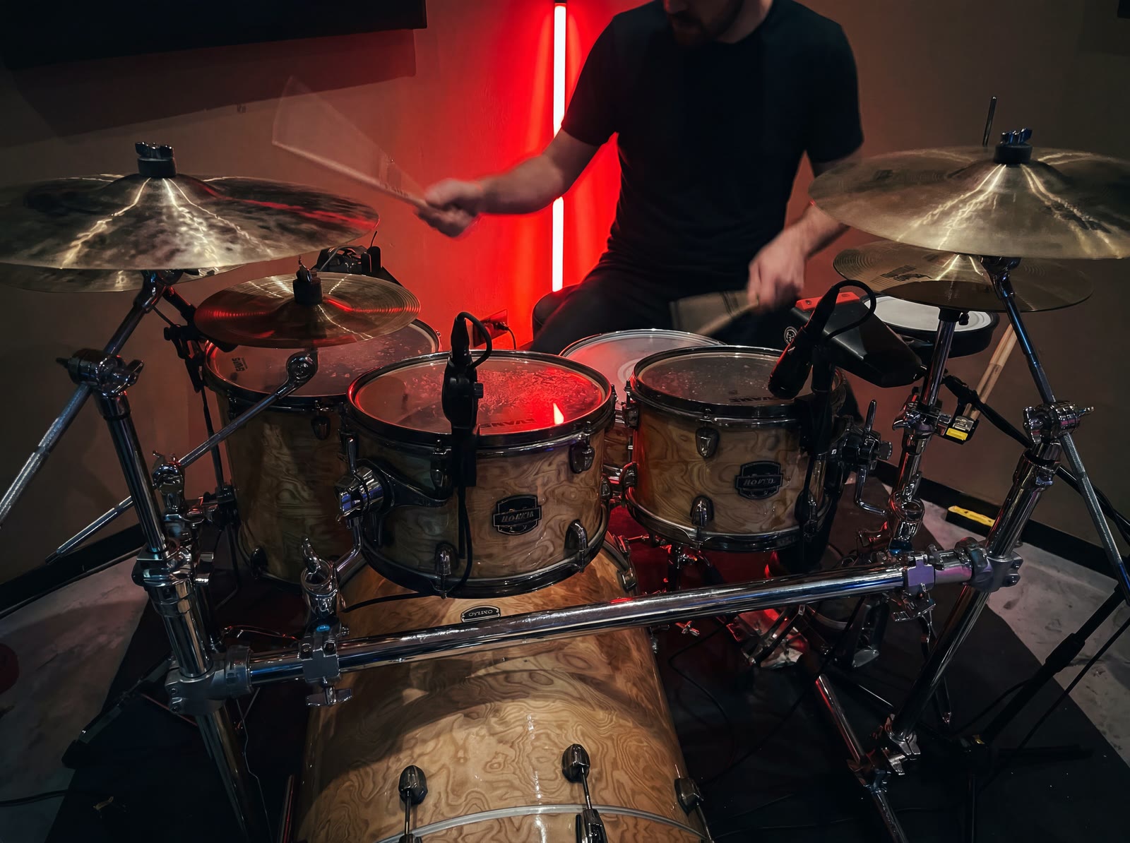 Een solodrummer die onder rood licht op een drumstel speelt bij Temple Studios